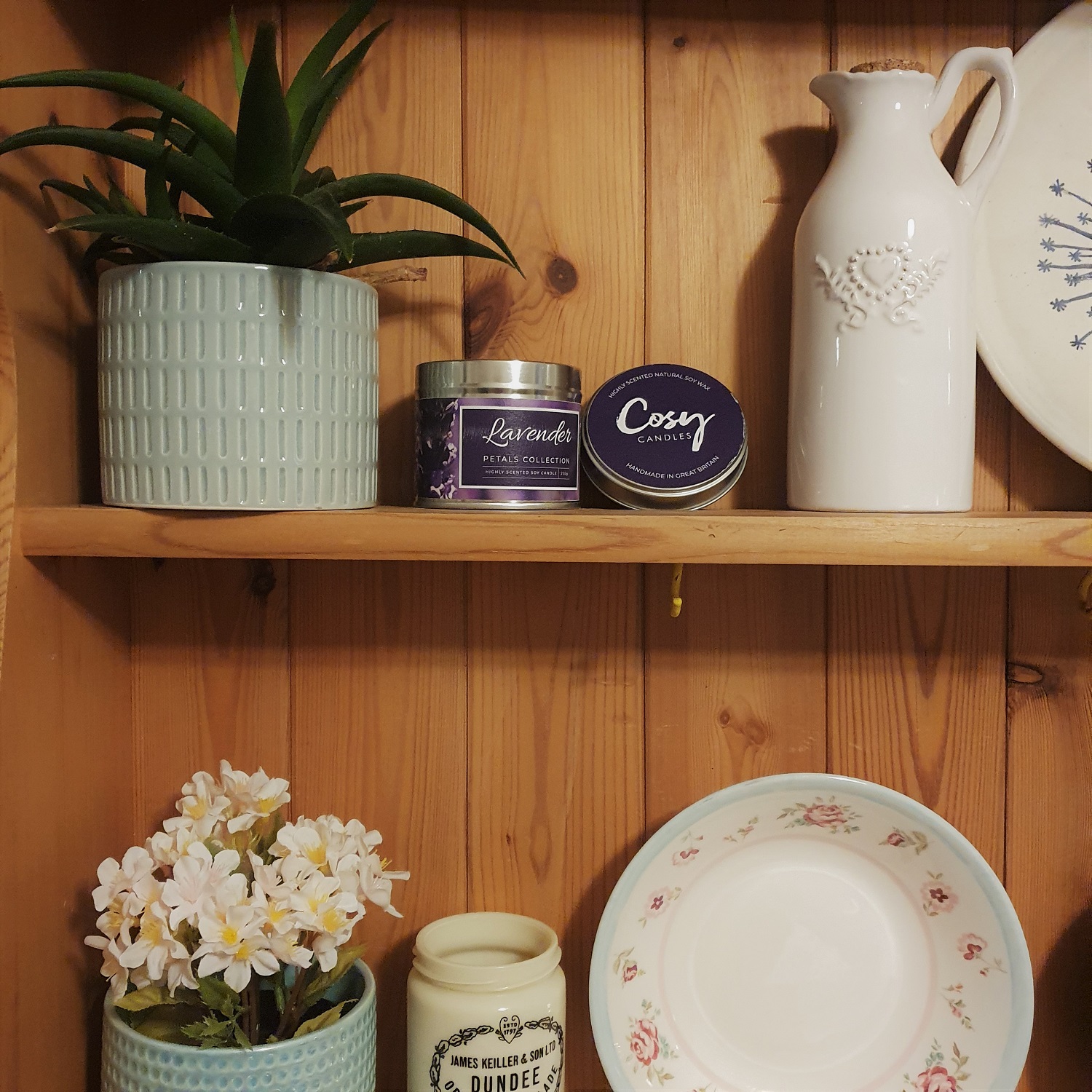 A shelf with assorted home decor and a Cosy Aromas candle
